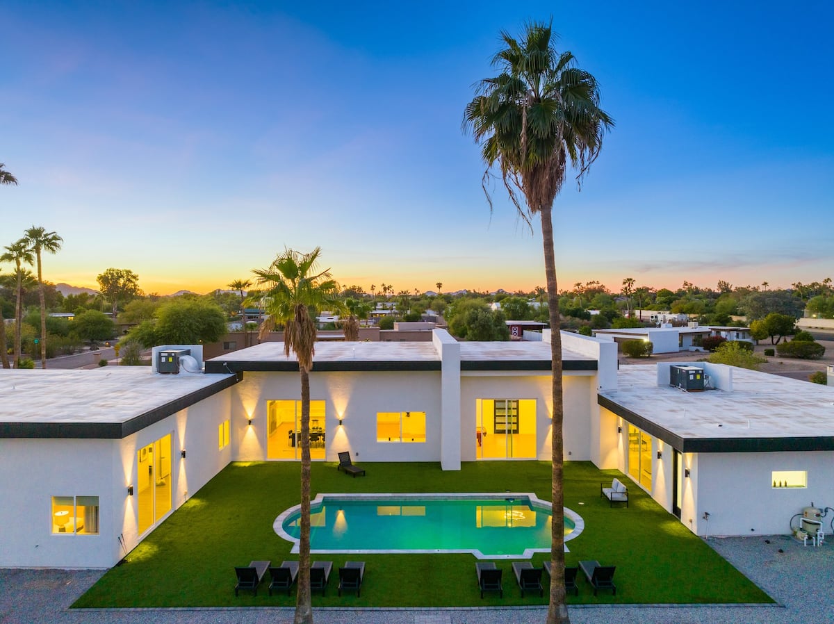 Aerial view of a modern home at dusk with a pool surrounded by lush turf and palm trees
