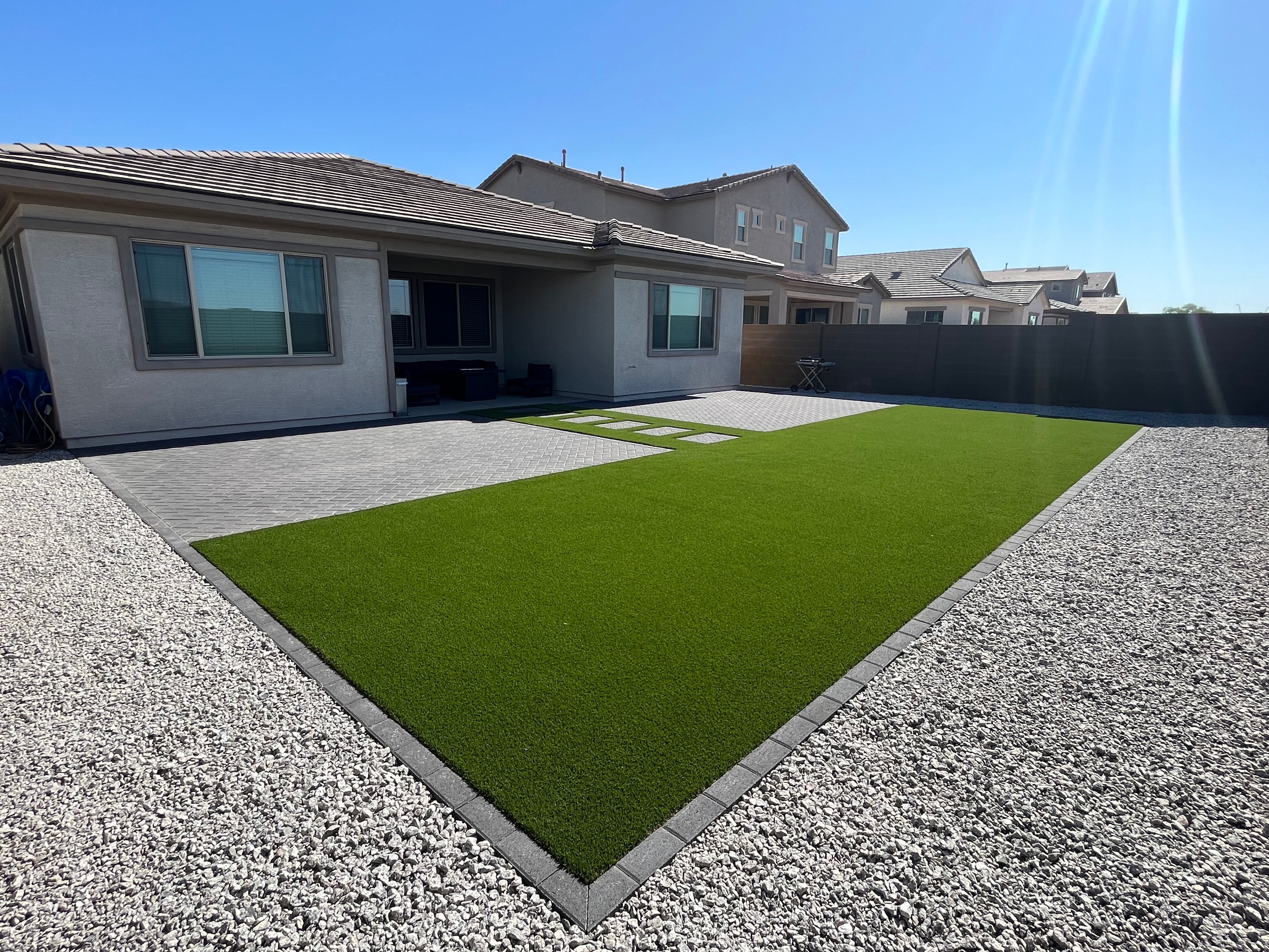 Finished backyard with a clean turf lawn bordered by pavers and gravel
