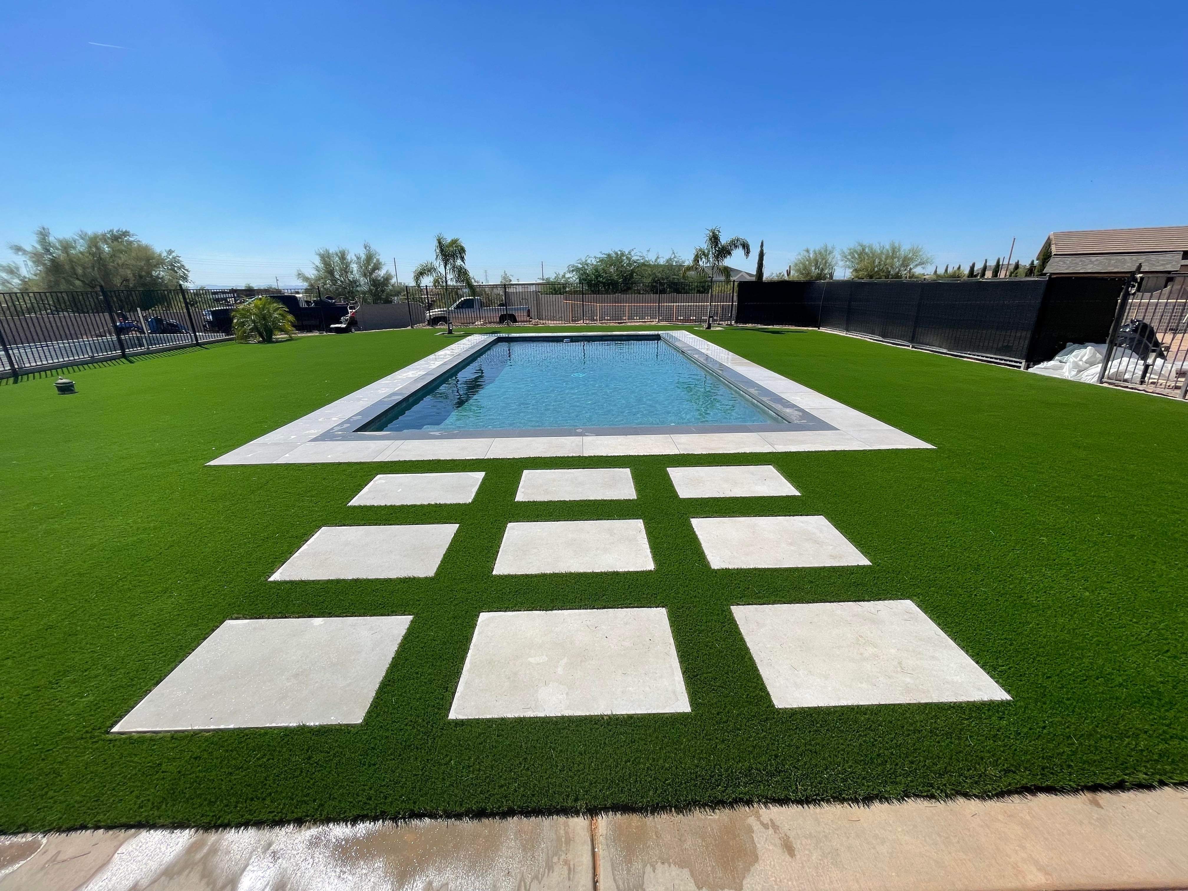 Rectangular pool surrounded by lush turf with checkerboard stone stepping pads