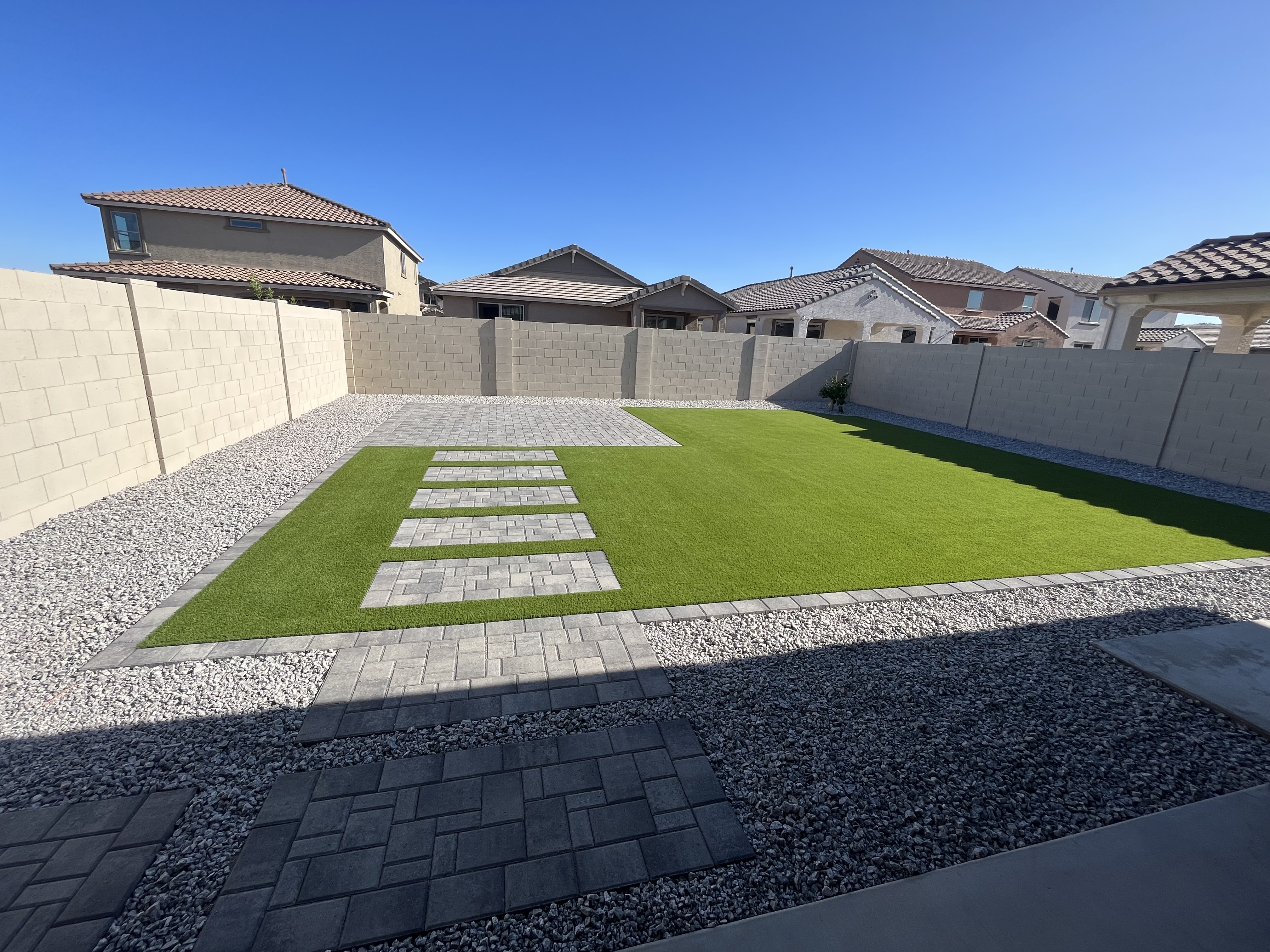 Turf lawn with a paver walkway and gravel borders between block walls